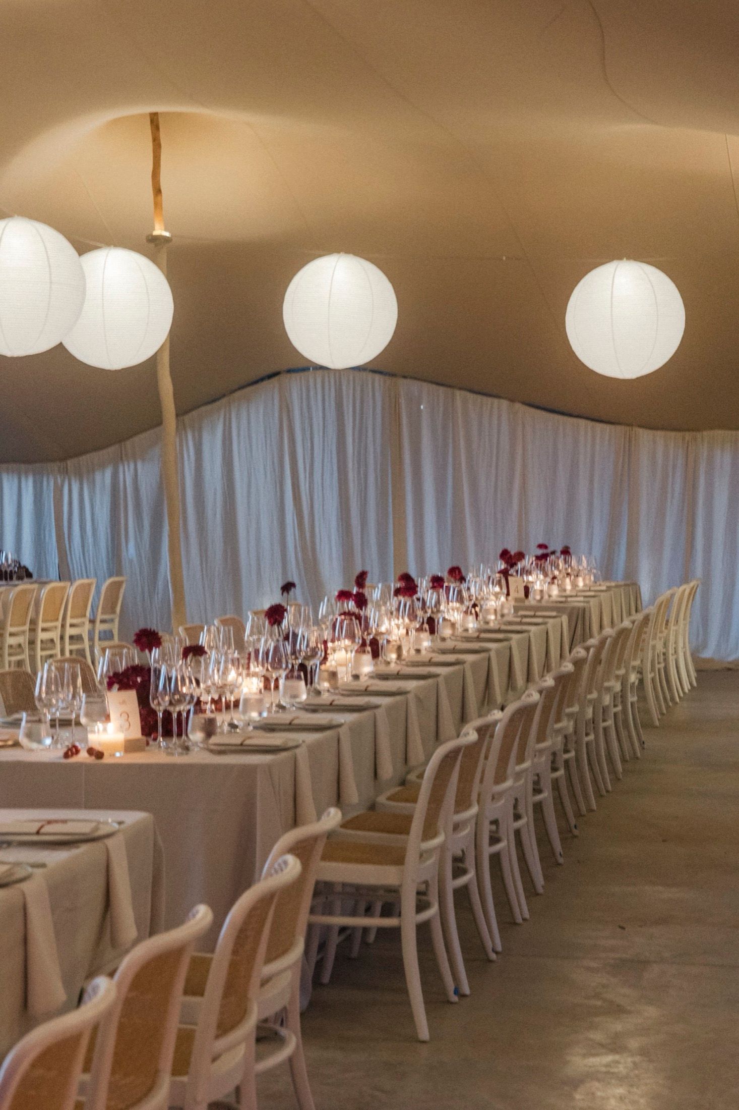 Elegant wedding reception venue with long white tables, paper lanterns, and sheer curtains creating a romantic atmosphere.