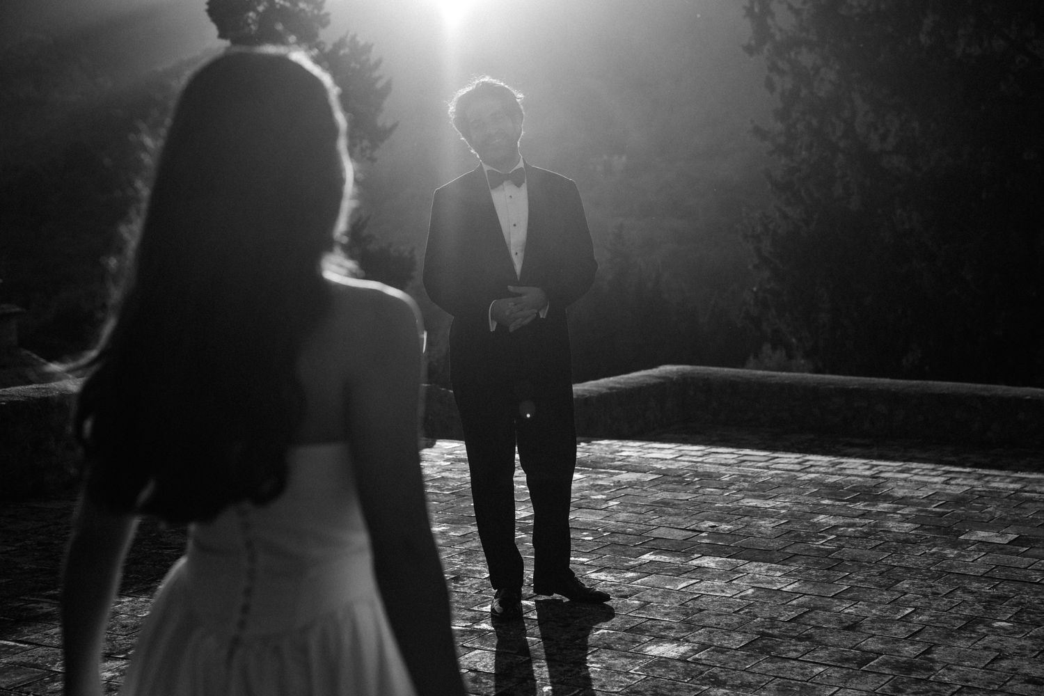 A dramatic black and white wedding moment captured in backlit silhouette during an outdoor ceremony.