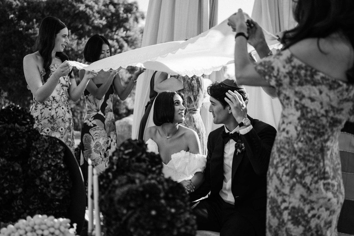 Black and white wedding photos show couple embracing under a floral arch during outdoor ceremony.