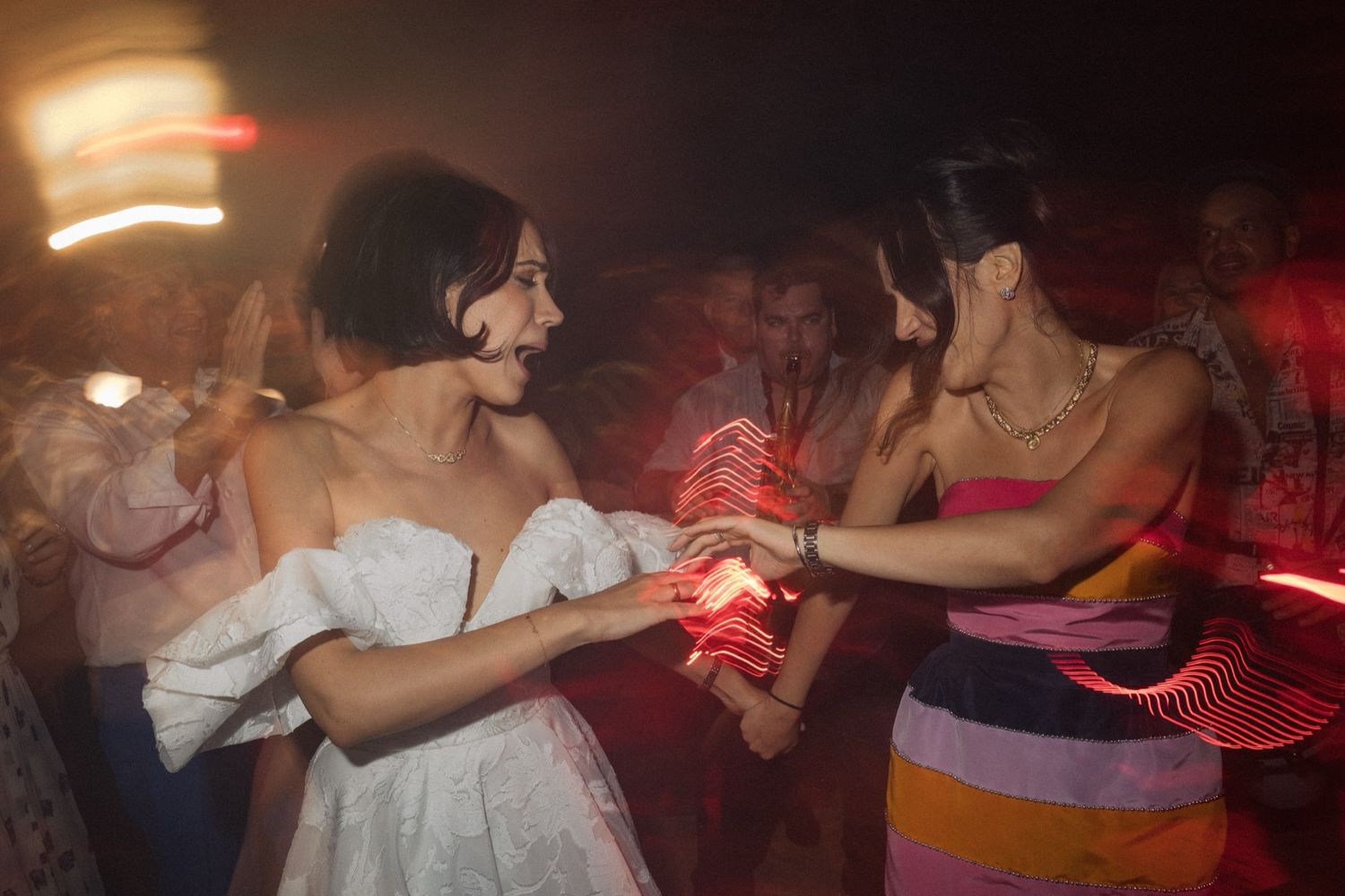 A dimly lit dance floor with people dancing and red lighting effects creating an energetic nightclub atmosphere.