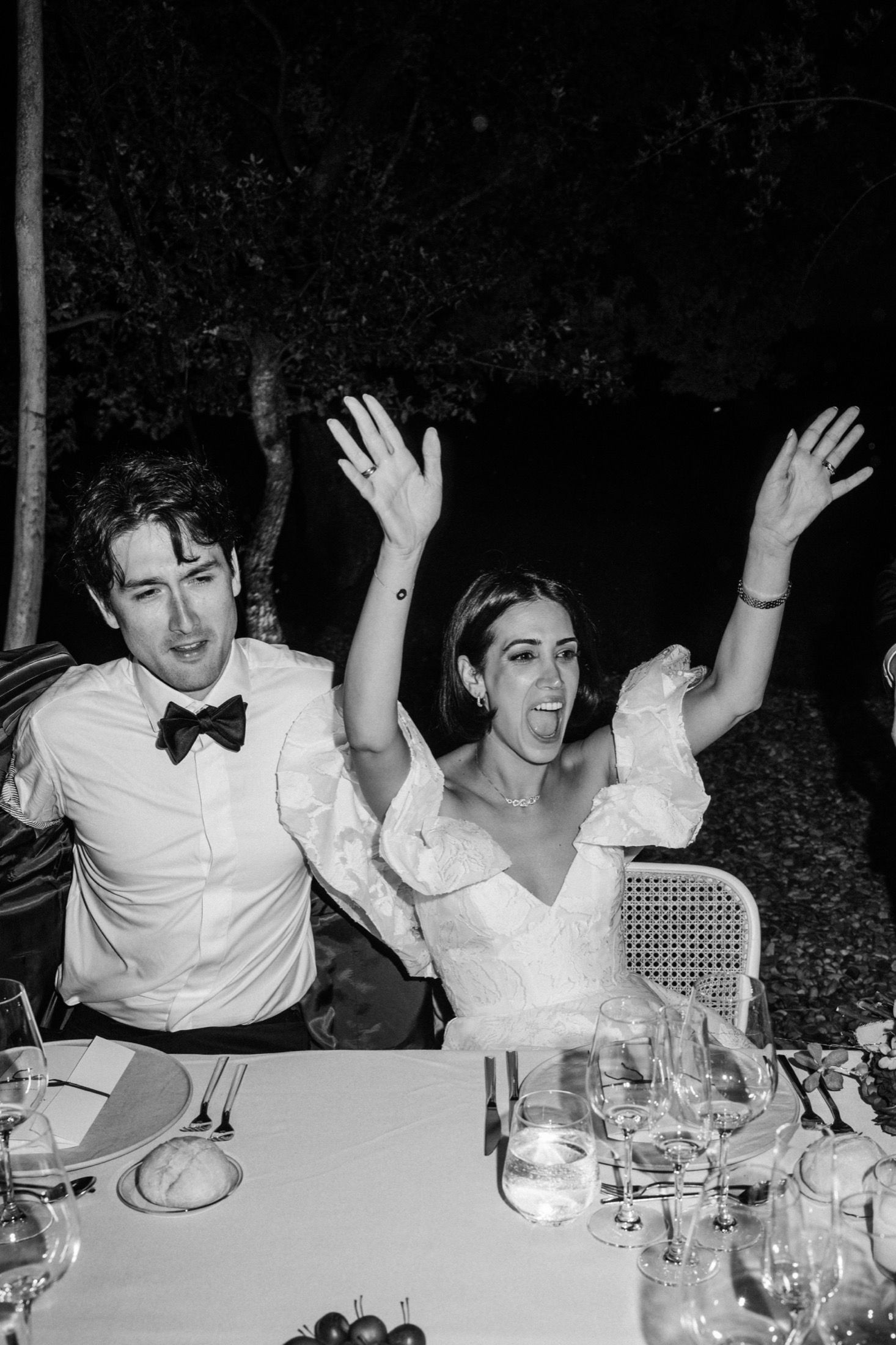 A joyful celebration moment at a wedding reception dinner with guests raising their arms in excitement.