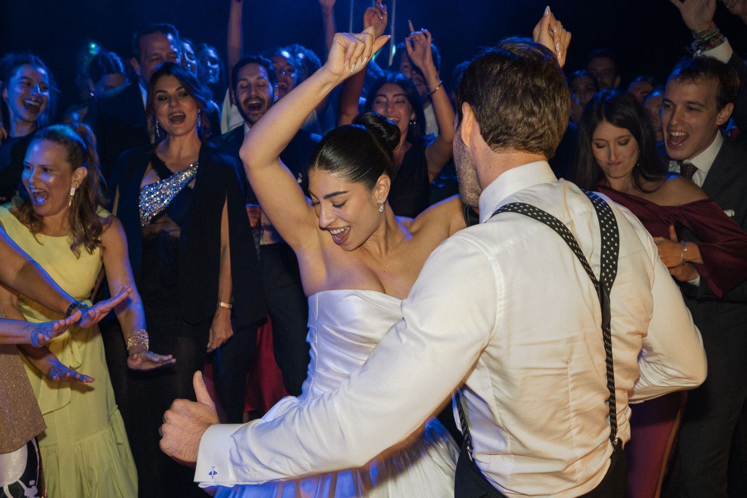 Couple dancing energetically at a wedding reception with guests watching and celebrating in the background.