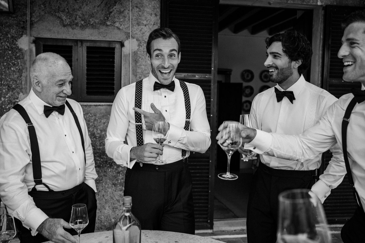 Black and white photo of a group of men in formal attire sharing drinks and laughing together at a celebration.