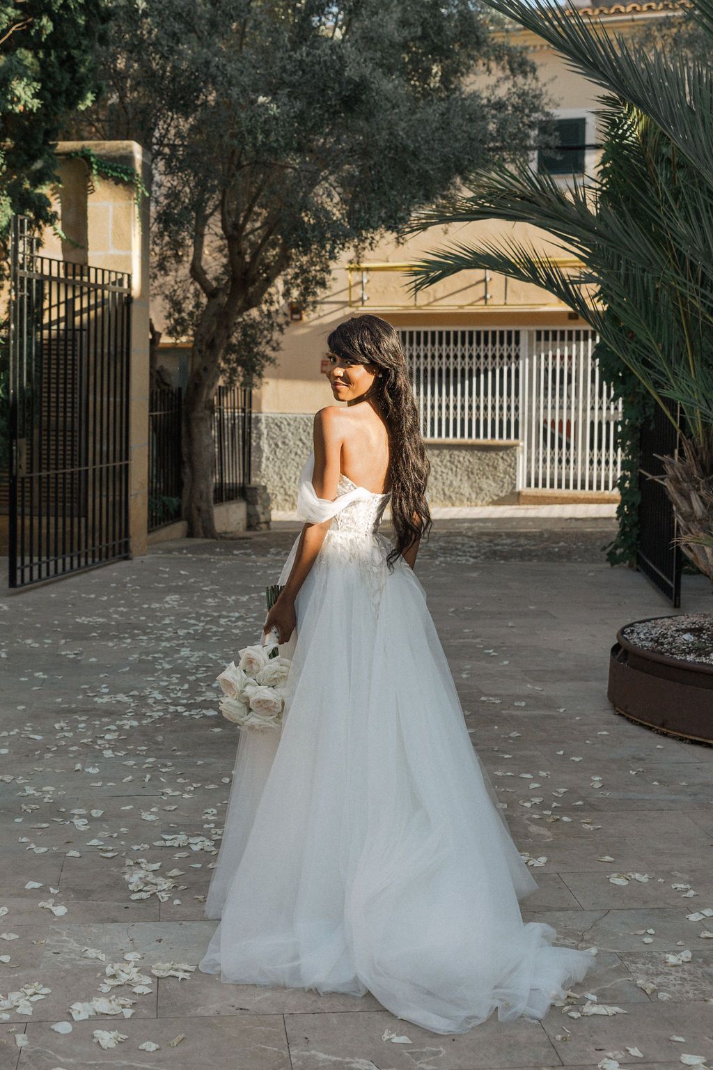 Bride in flowing white gown twirls gracefully on stone patio surrounded by greenery.