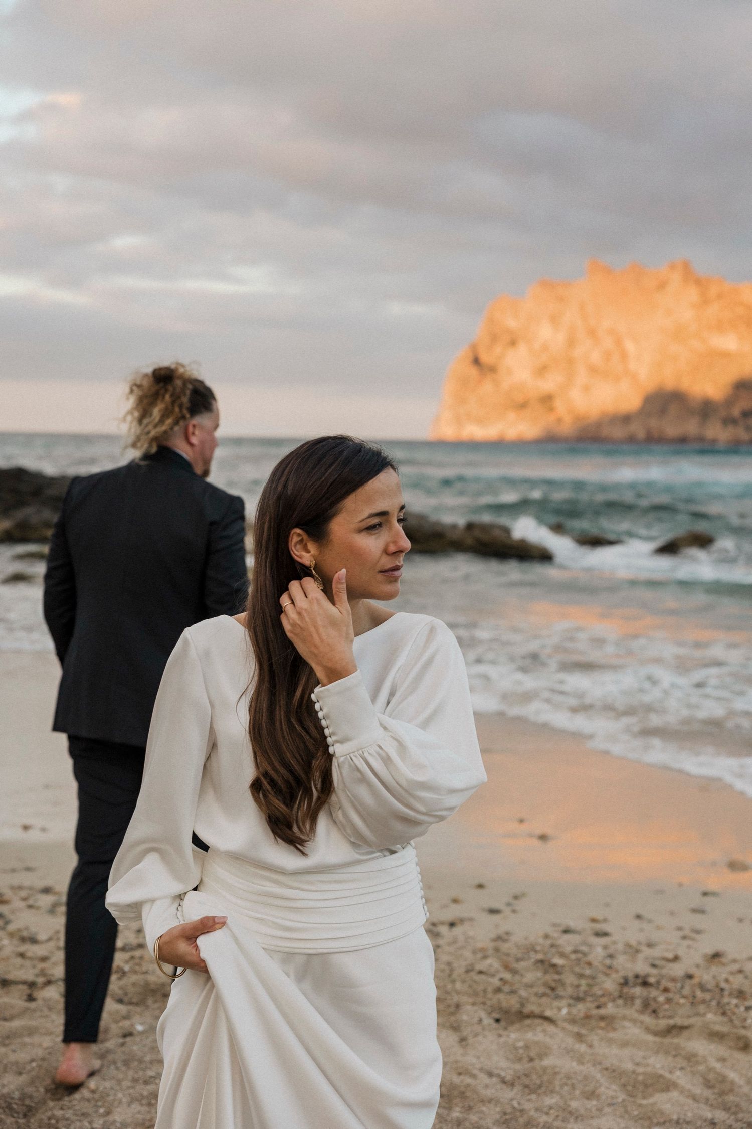 Coastal wedding photo with golden cliffs and ocean backdrop at sunset.