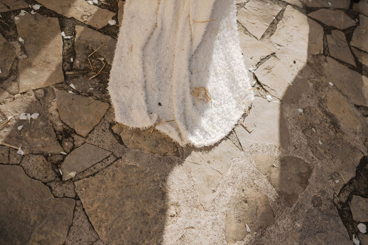 Close-up detail of white wedding dress train trailing on stone ground.