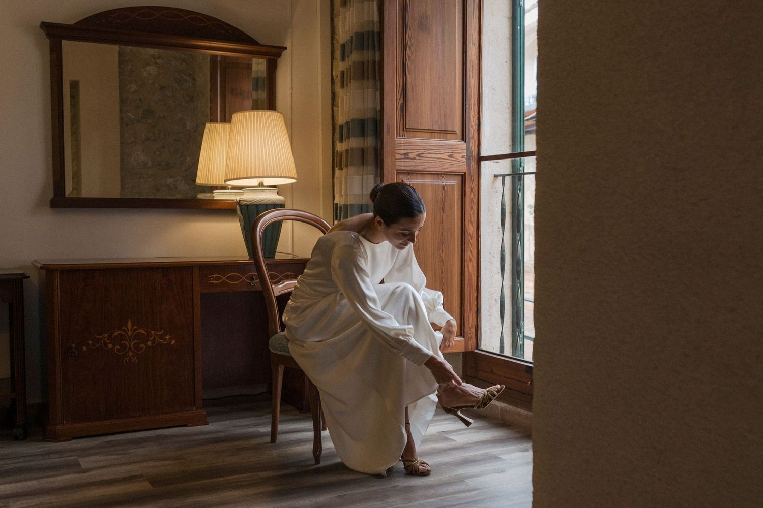 Natural light illuminates a room where a white dress creates elegant shadows against wooden details.