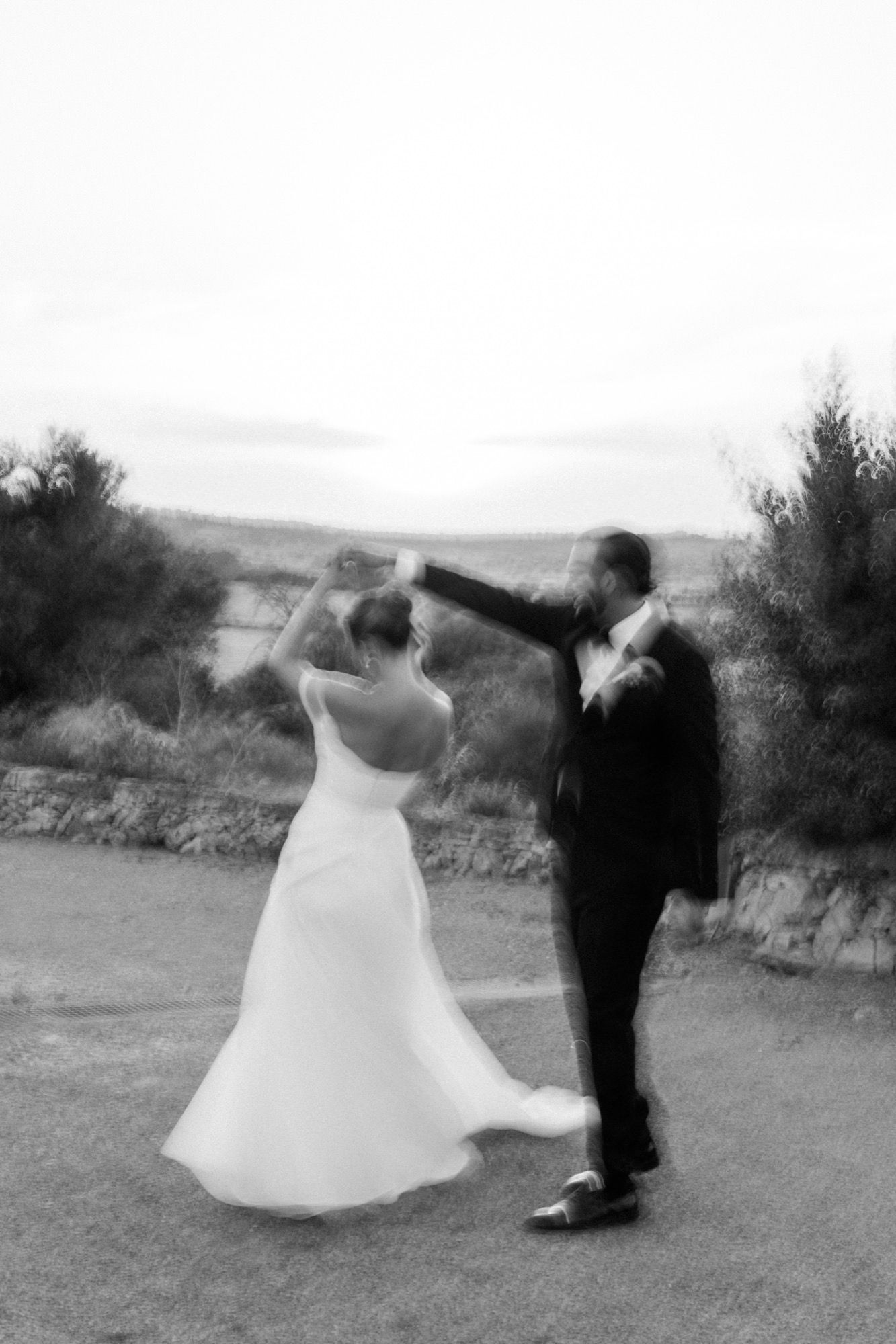 Motion blur captures dancing newlyweds in black and white against outdoor setting.
