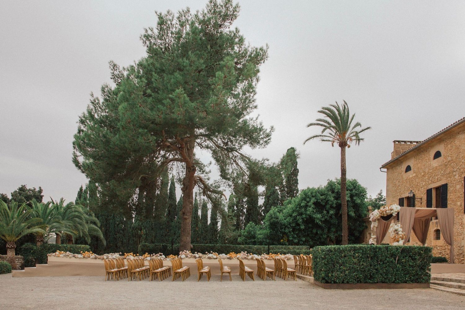 A panoramic view of a desert resort with palm trees, wooden lounge chairs, and rustic architecture against a sandy landscape.