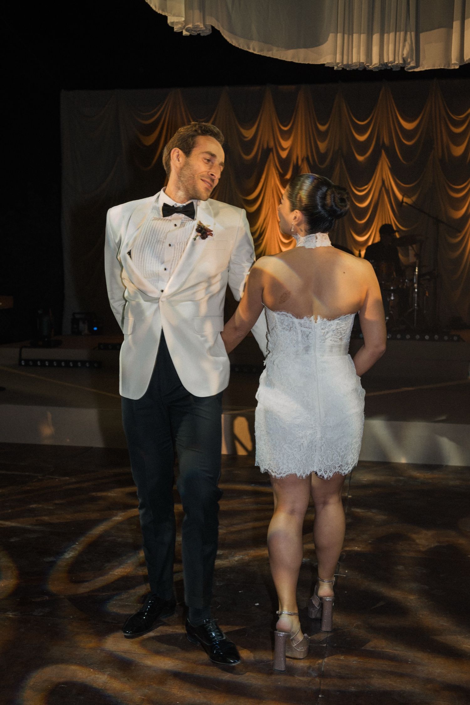 Couple dancing together at a formal event on a patterned dance floor with gold curtains in the background.