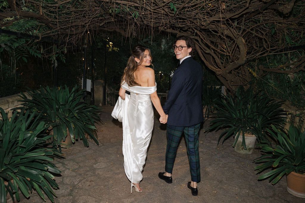 Couple walking through lush garden pathway at night in formal attire.