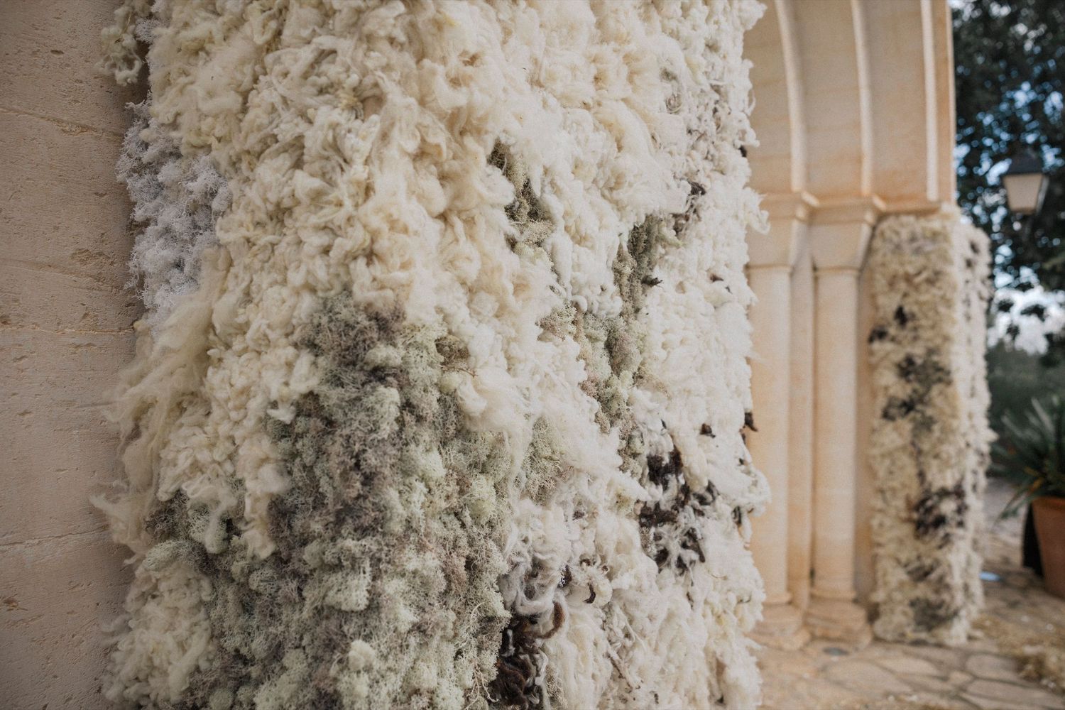 White floral arrangements with cascading blooms adorn elegant stone pillars at an outdoor wedding venue.