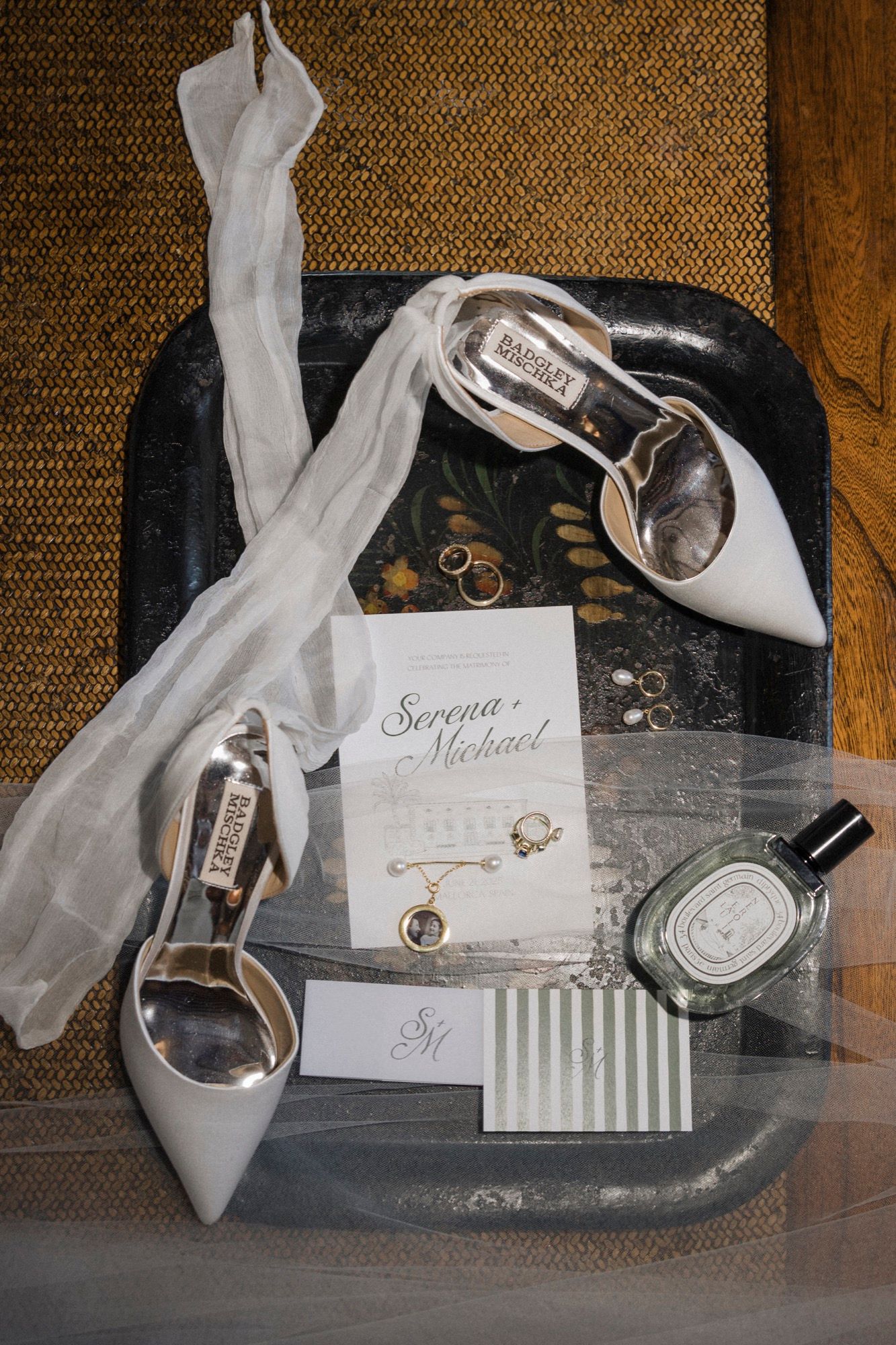 Wedding accessories including white shoes and invitation cards arranged on a dark surface.