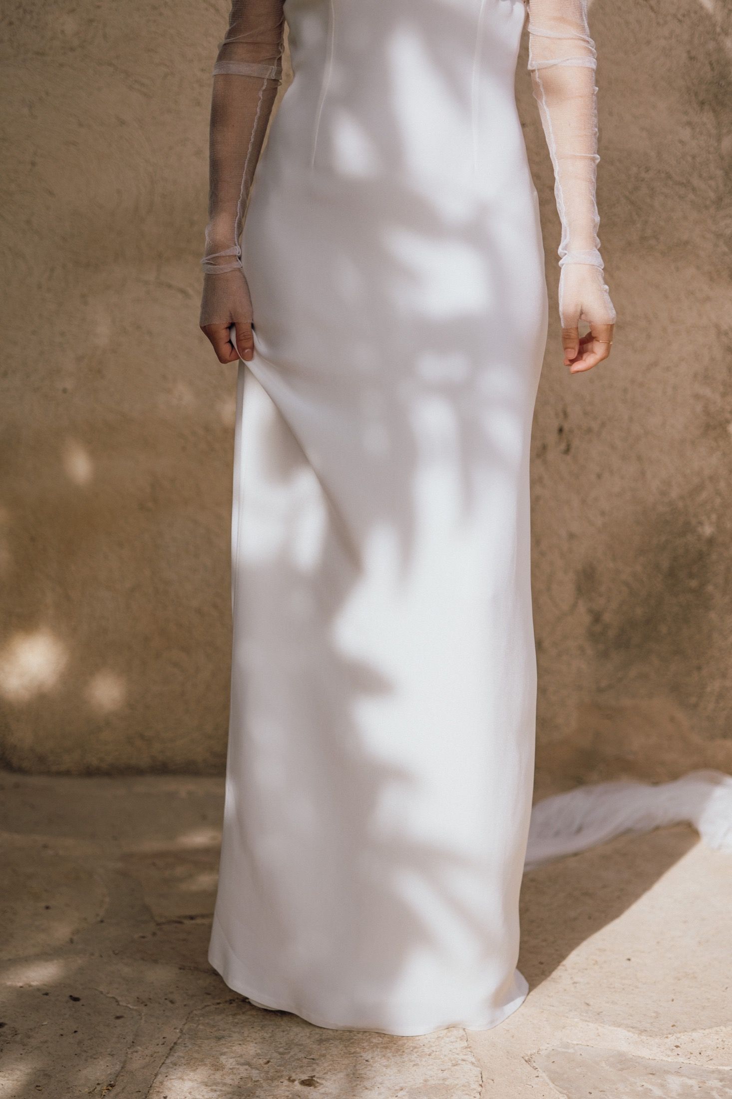 Minimalist white dress details shown in a series of cropped photos against a textured beige wall with dappled lighting.