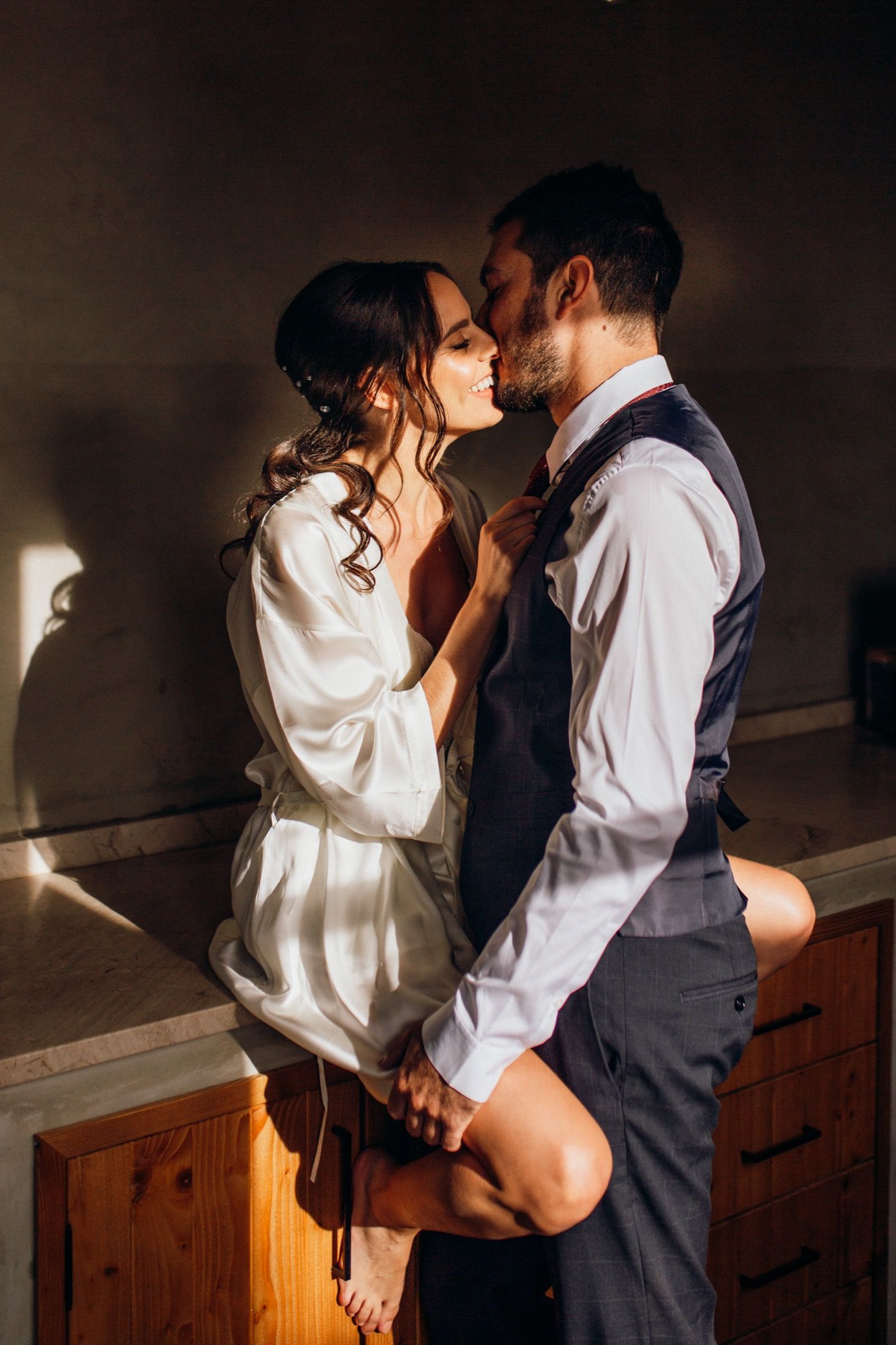 Romantic couple in intimate embrace wearing white shirt and dark vest share tender moments in a dimly lit room.