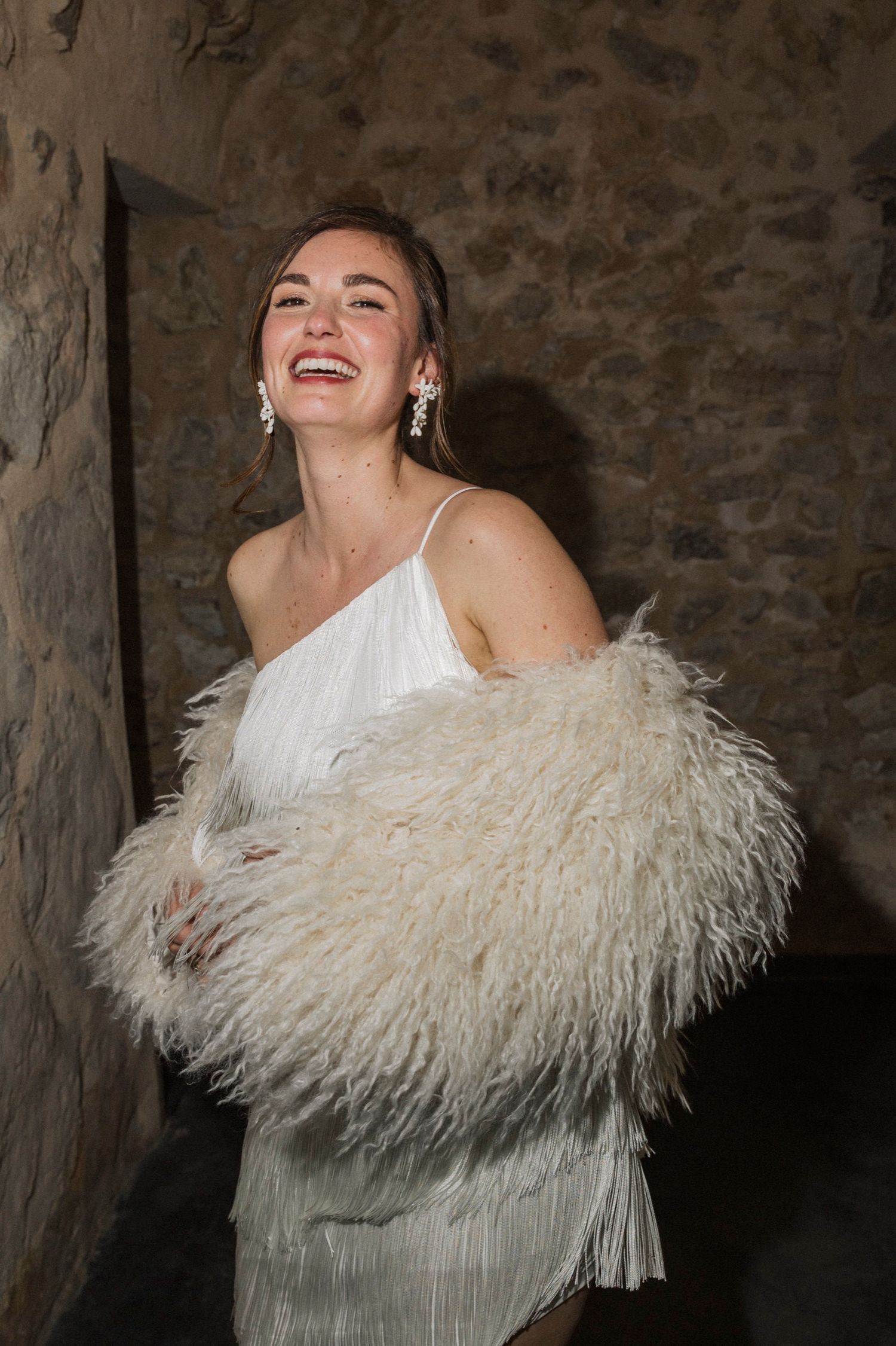 A joyful moment captured in a white dress and luxurious feathered wrap against a stone wall background.