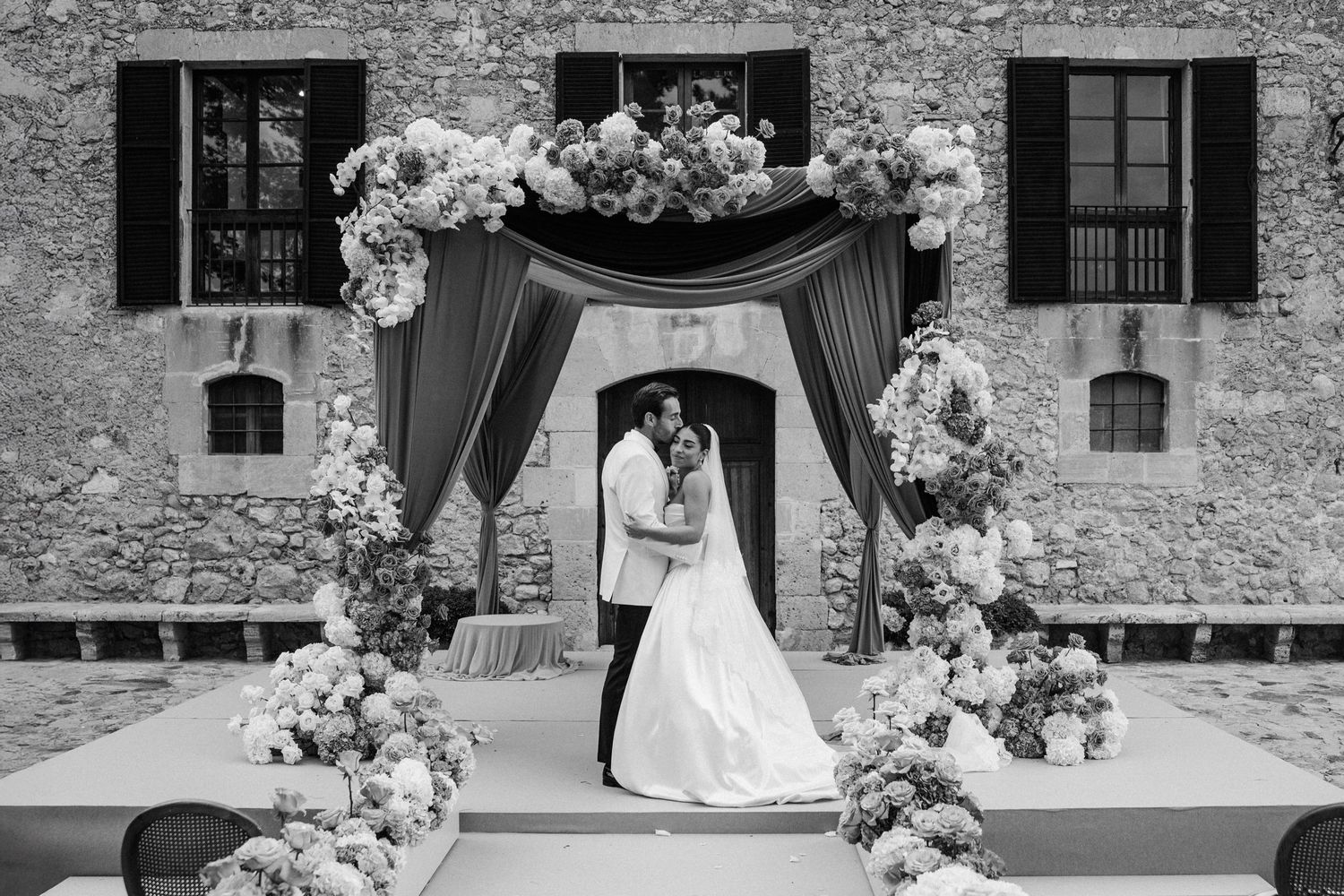Black and white wedding photos showing couples in romantic poses at a rustic stone venue with elegant floral arrangements.