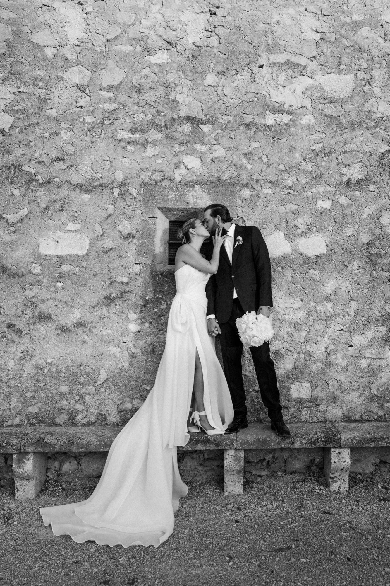 Black and white wedding photos showing couple's playful interactions along an old stone wall.