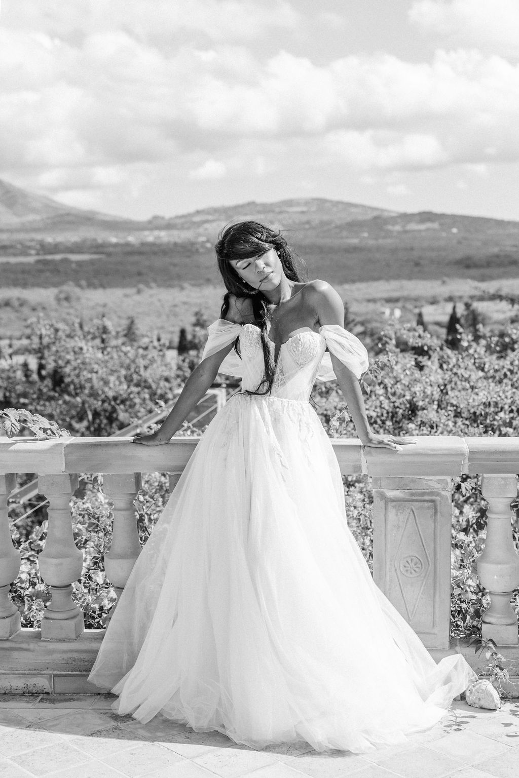 Black and white photo of a flowing wedding gown on a balcony with mountain views.