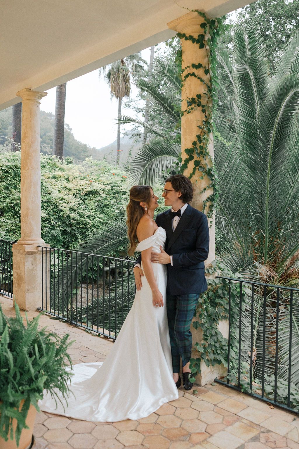 Elegant wedding portraits on stone terrace with tropical foliage and white columns.