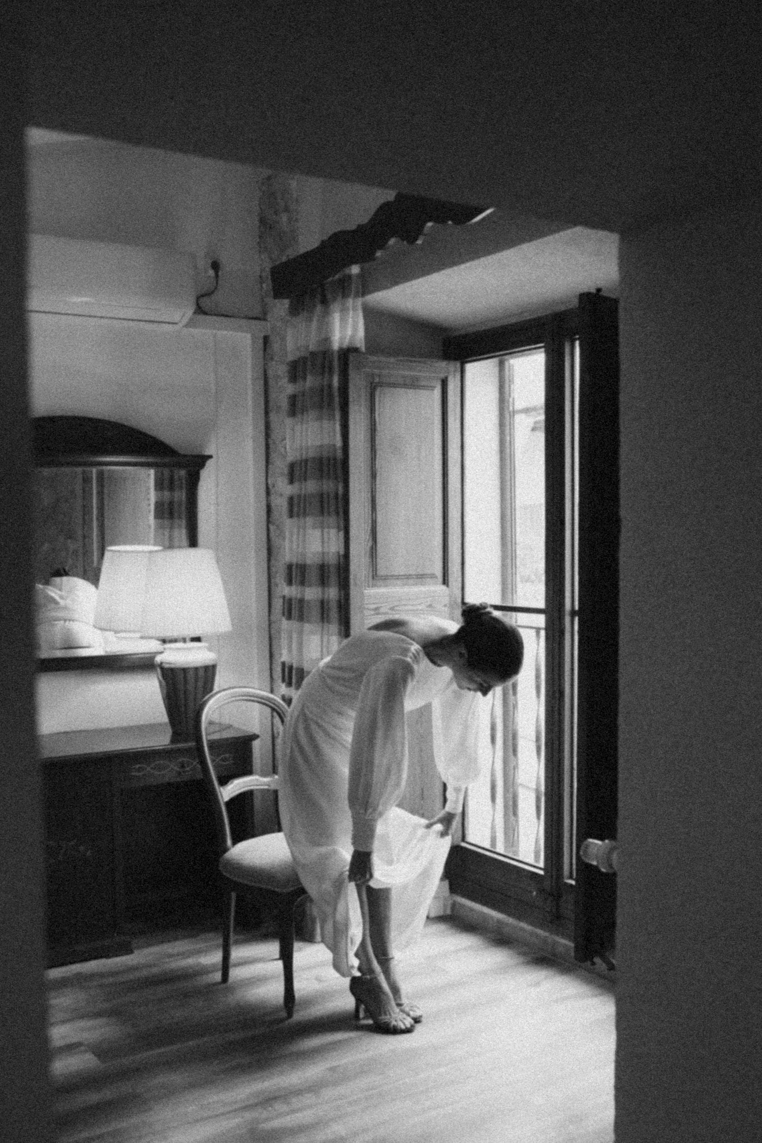 A black and white photo captures movement of a white dress near a window in an empty room.