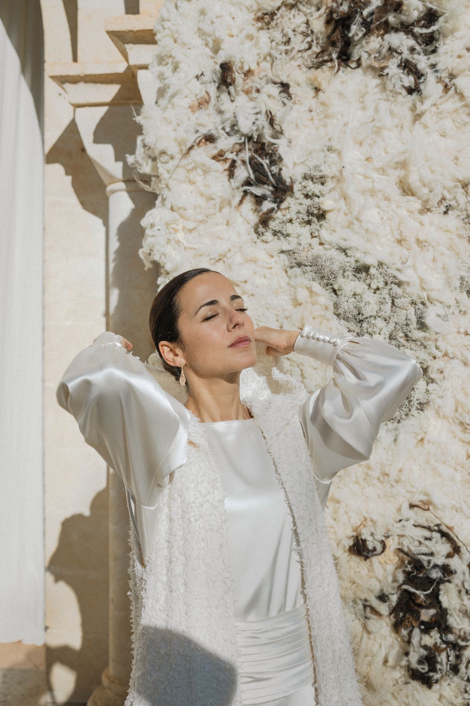 Elegant bridal portrait with white pearl-adorned dress against textured stone wall.