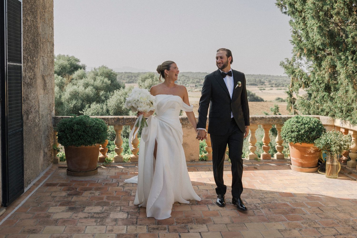 Elegant wedding couple poses on a sunny terrace overlooking a scenic landscape.