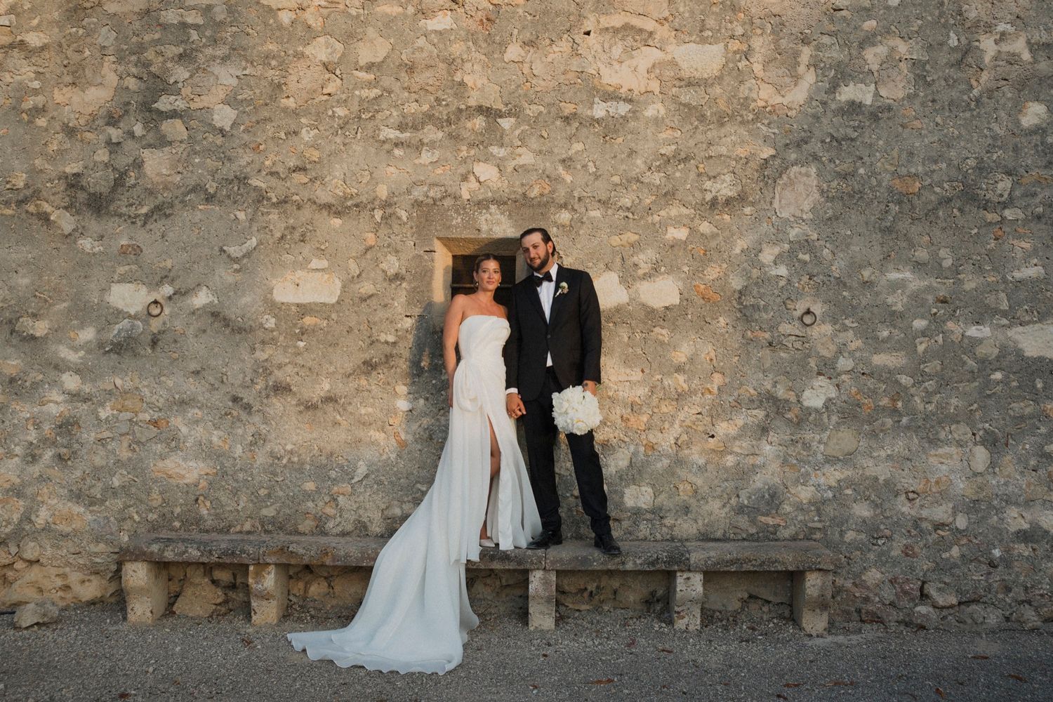 A wedding couple poses against a weathered stone wall in a series of romantic black and white photos.