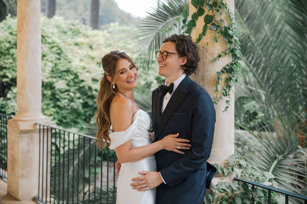 Newlyweds share intimate moments on a tropical veranda with palm trees in background.