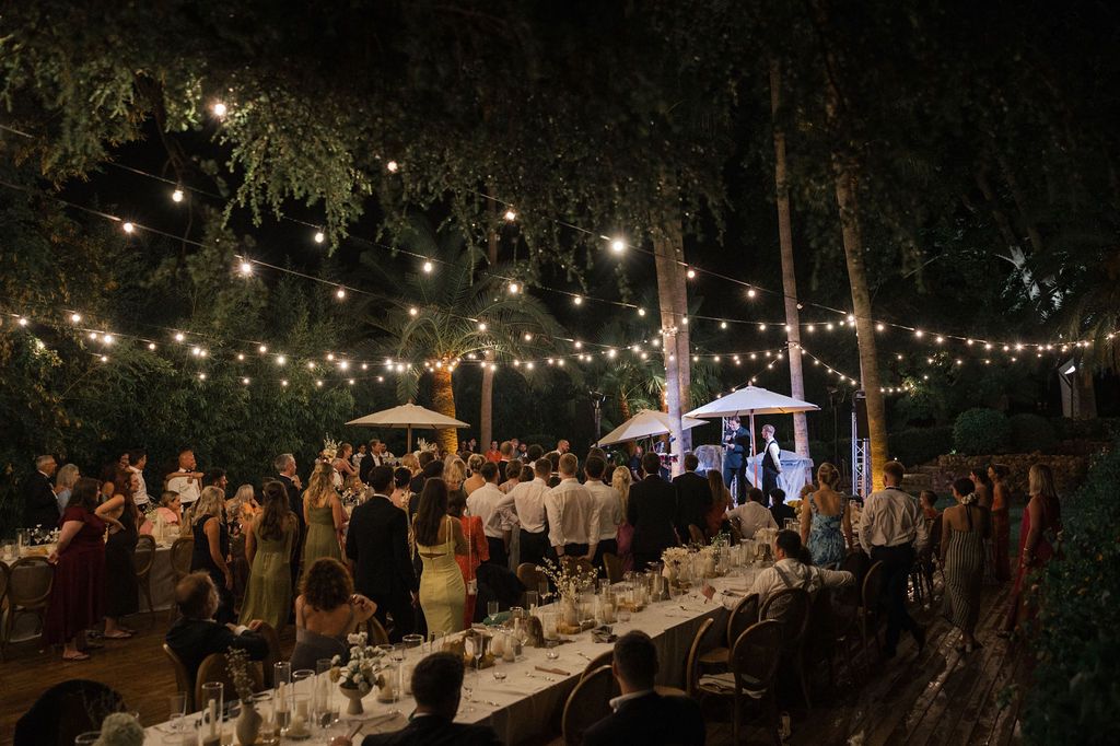 Outdoor wedding reception venue with string lights and long dining tables at night.