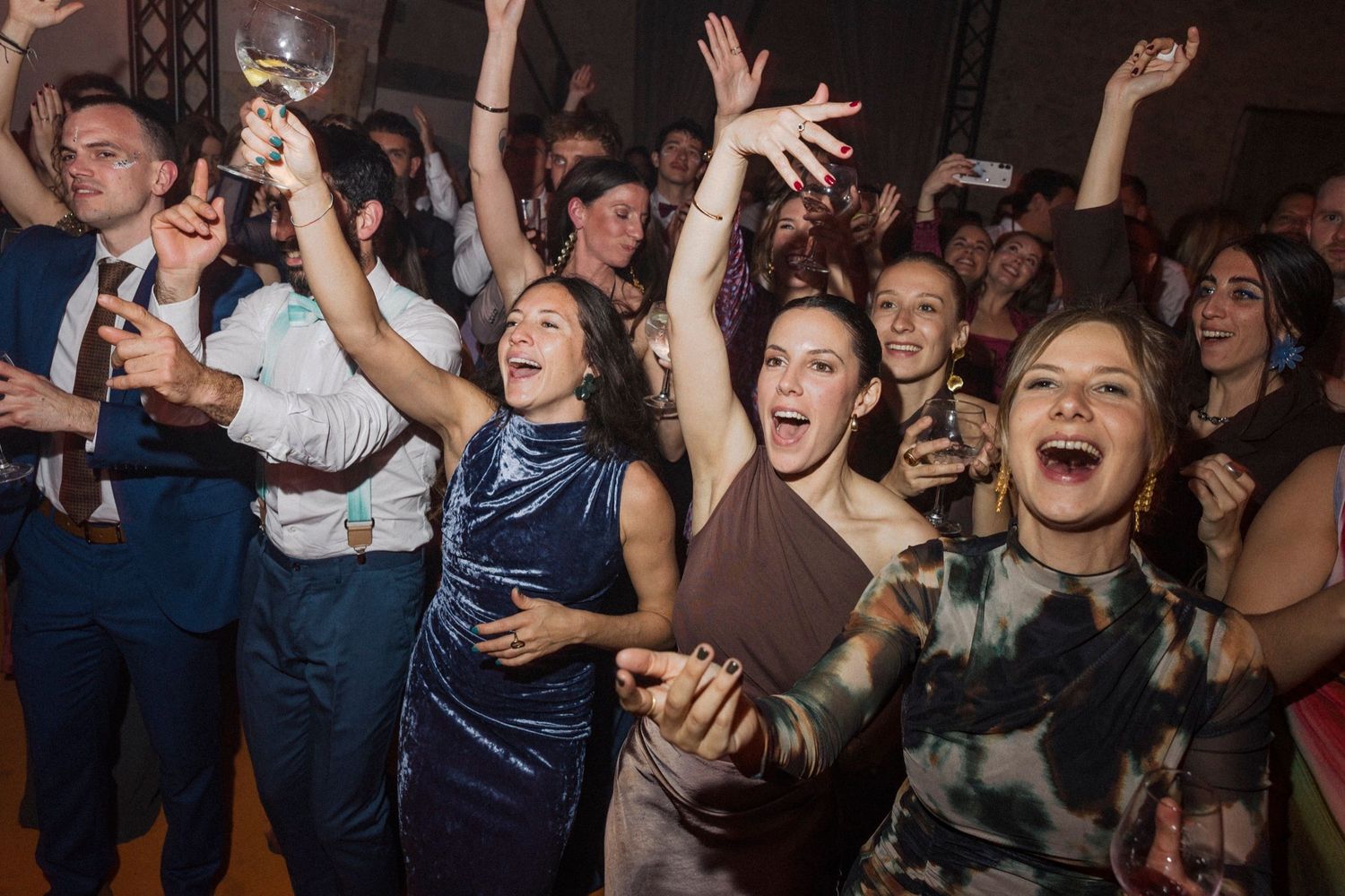 Crowd of excited concert attendees cheering and raising their hands in a dark venue with dramatic lighting.