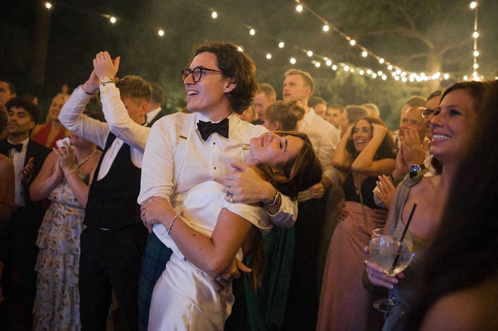 Guests enjoying a lively wedding reception with string lights illuminating the outdoor venue.