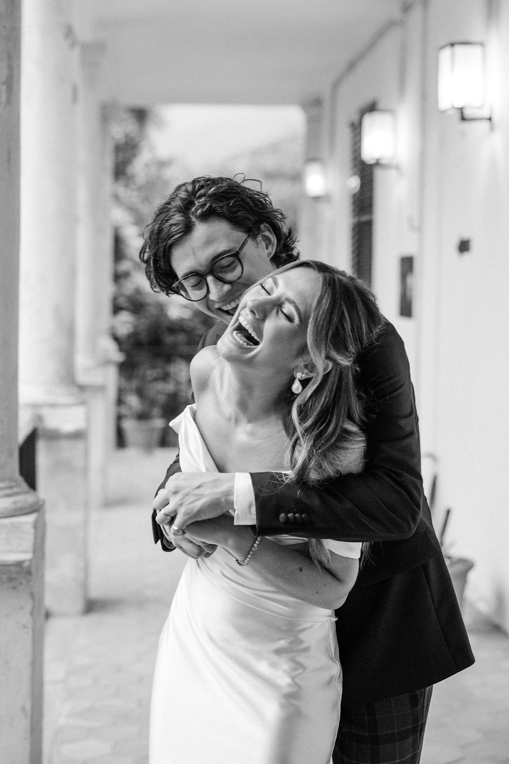 Black and white portrait of couple sharing intimate moment on columned porch.