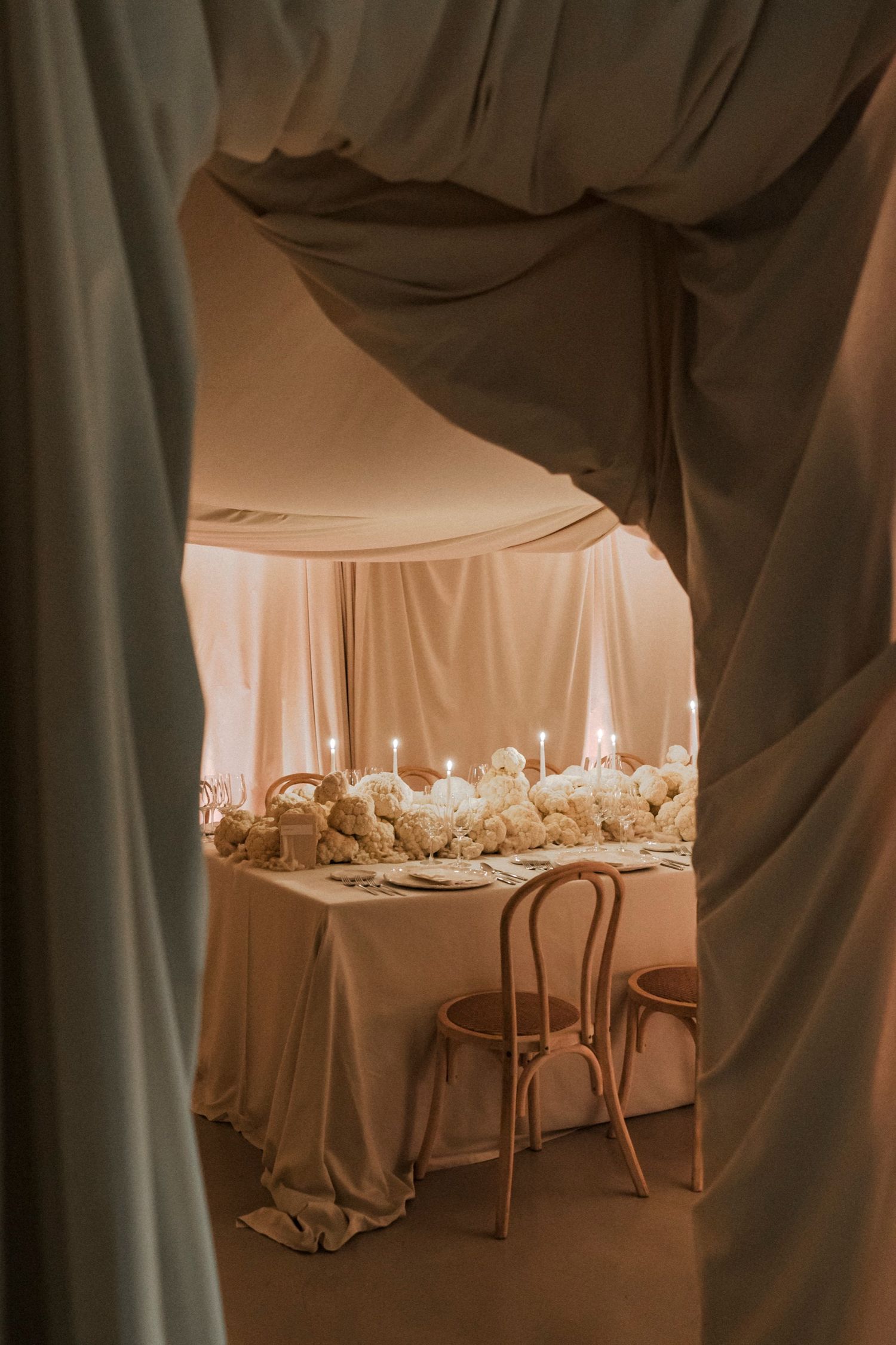 Romantic dining setup with draped fabric walls and elegant table settings in warm lighting.
