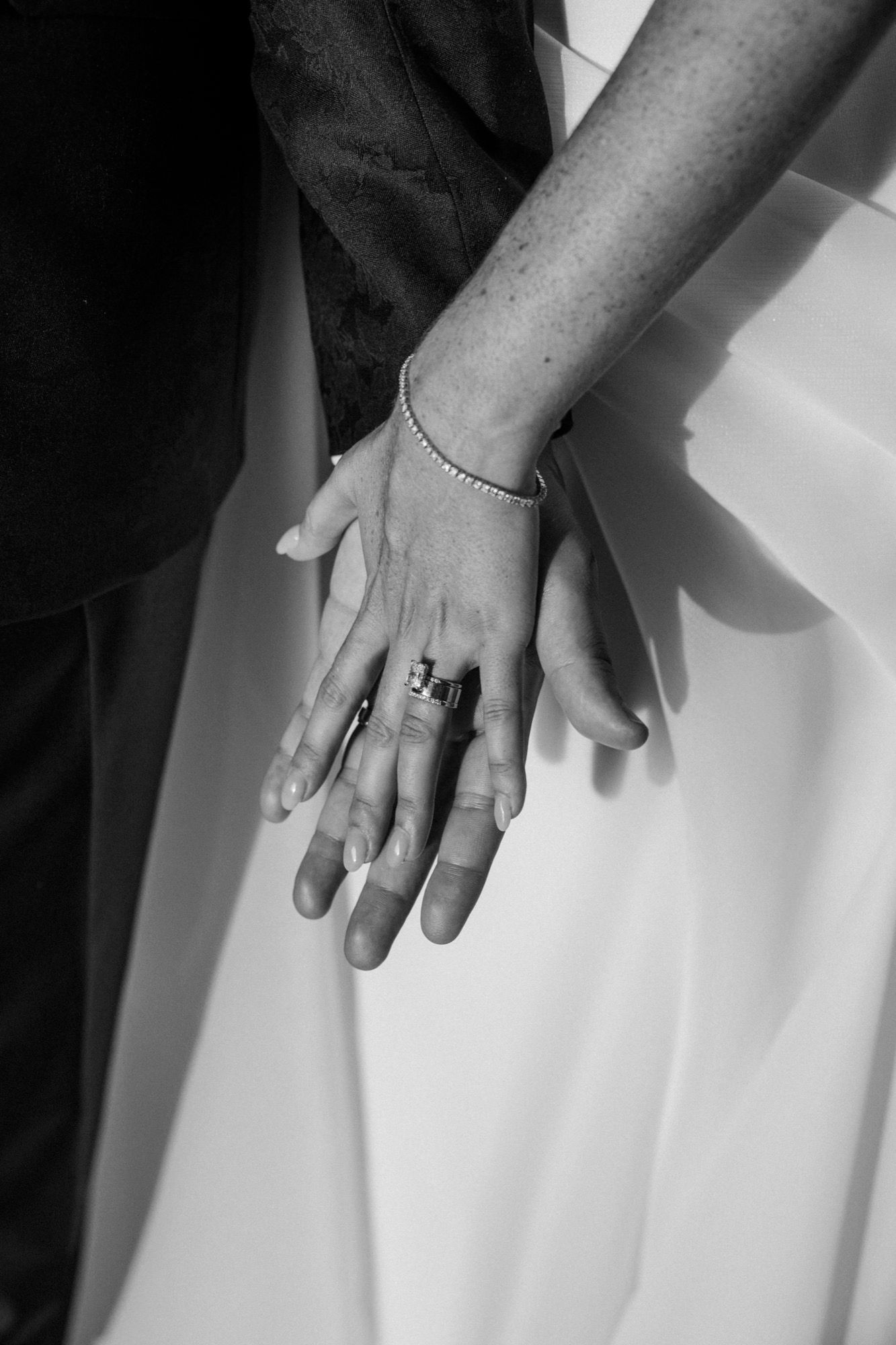 A black and white detail shot of hands with wedding rings and delicate bracelet.