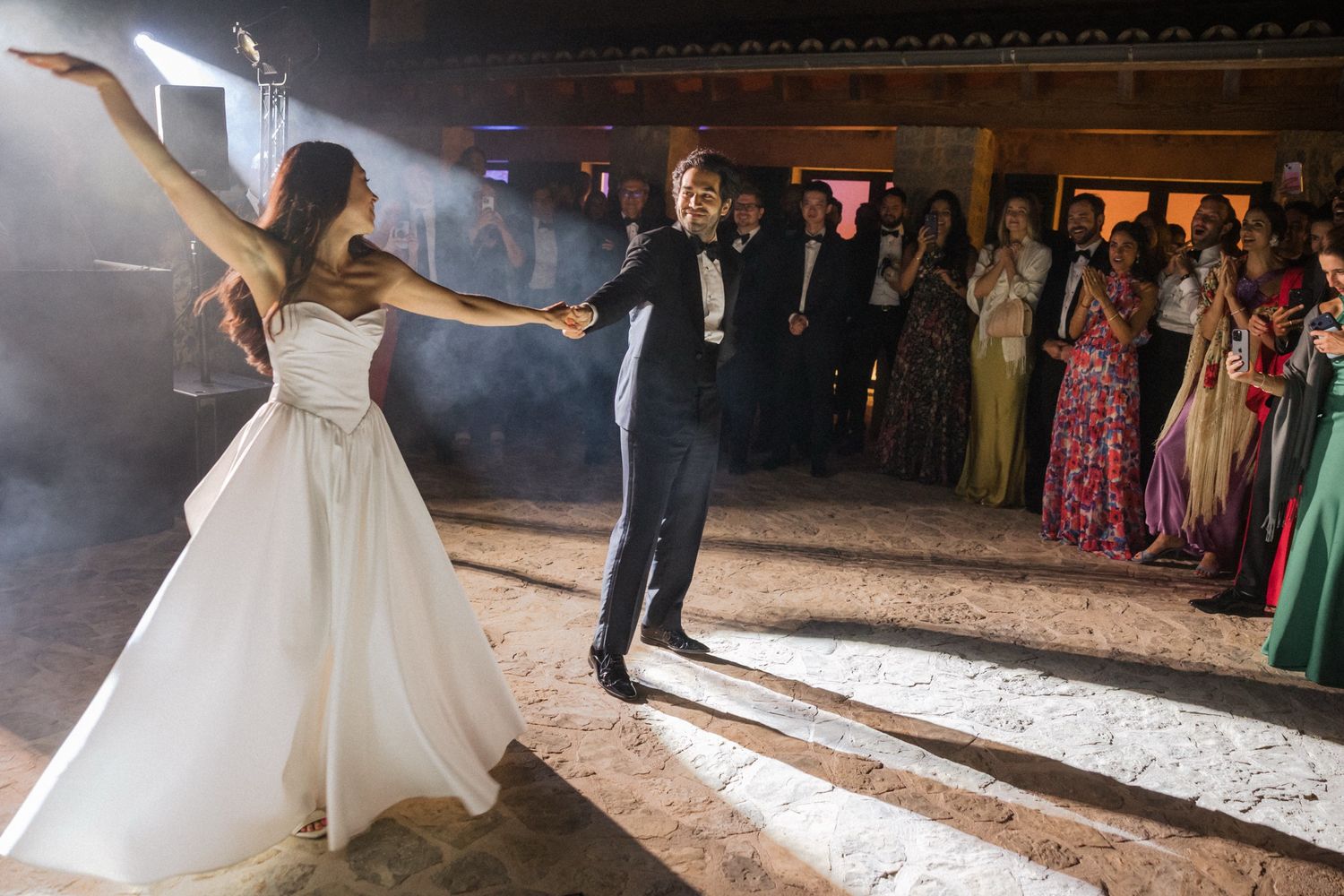 A couple performs their first dance at a wedding reception as guests watch from the sides of the dance floor.