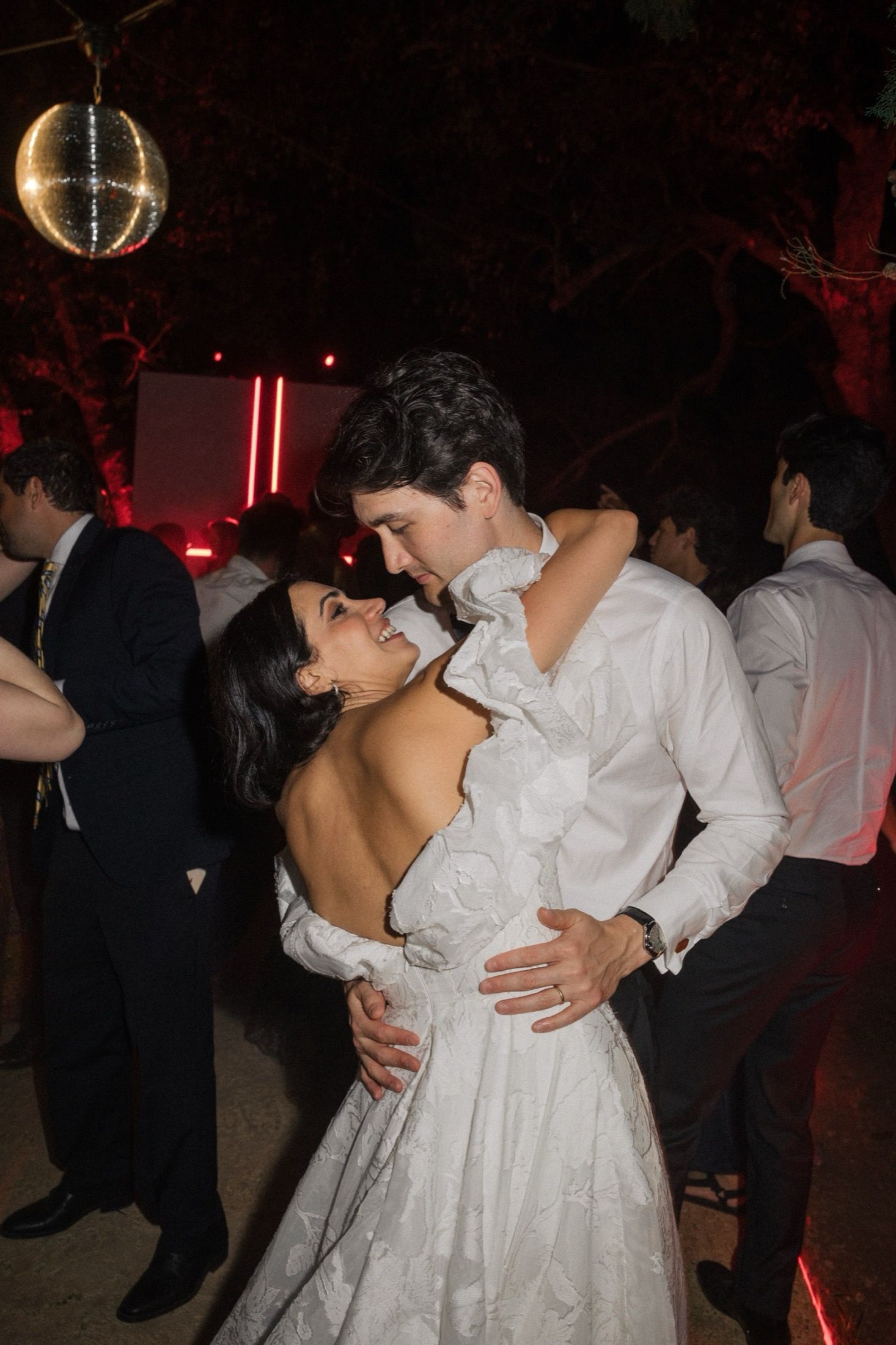 Couples slow dance together at a dimly lit wedding reception with romantic lighting and formal attire.
