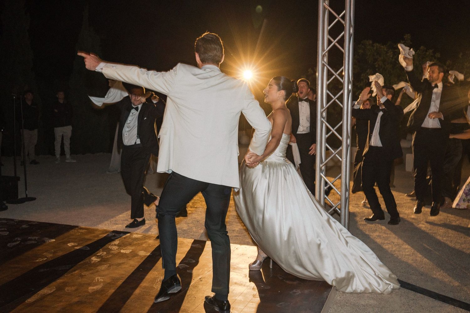 Wedding guests dance and celebrate on a dimly lit dance floor at an evening reception.