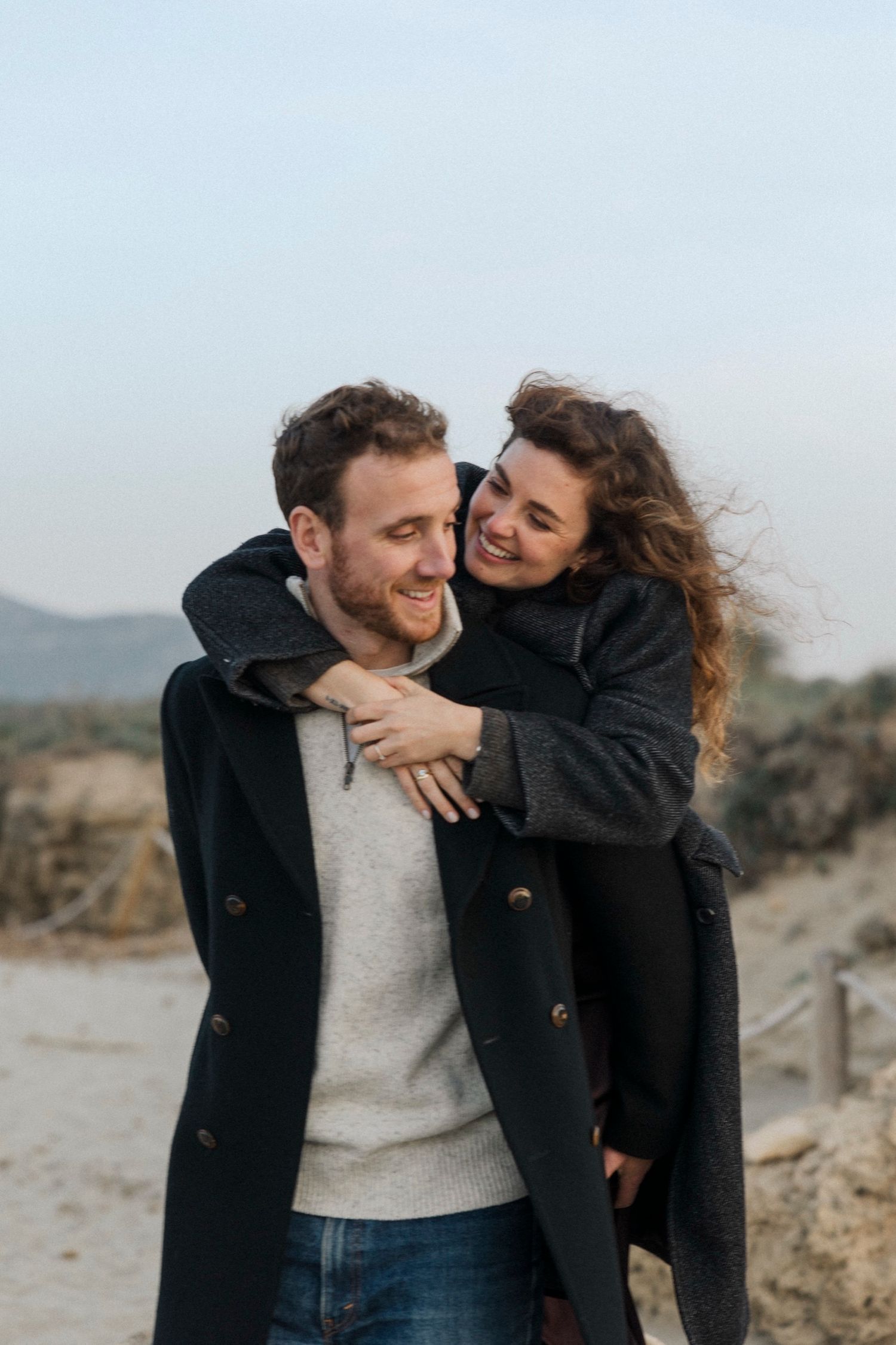 Joyful couple embracing and laughing together in a desert landscape during golden hour.