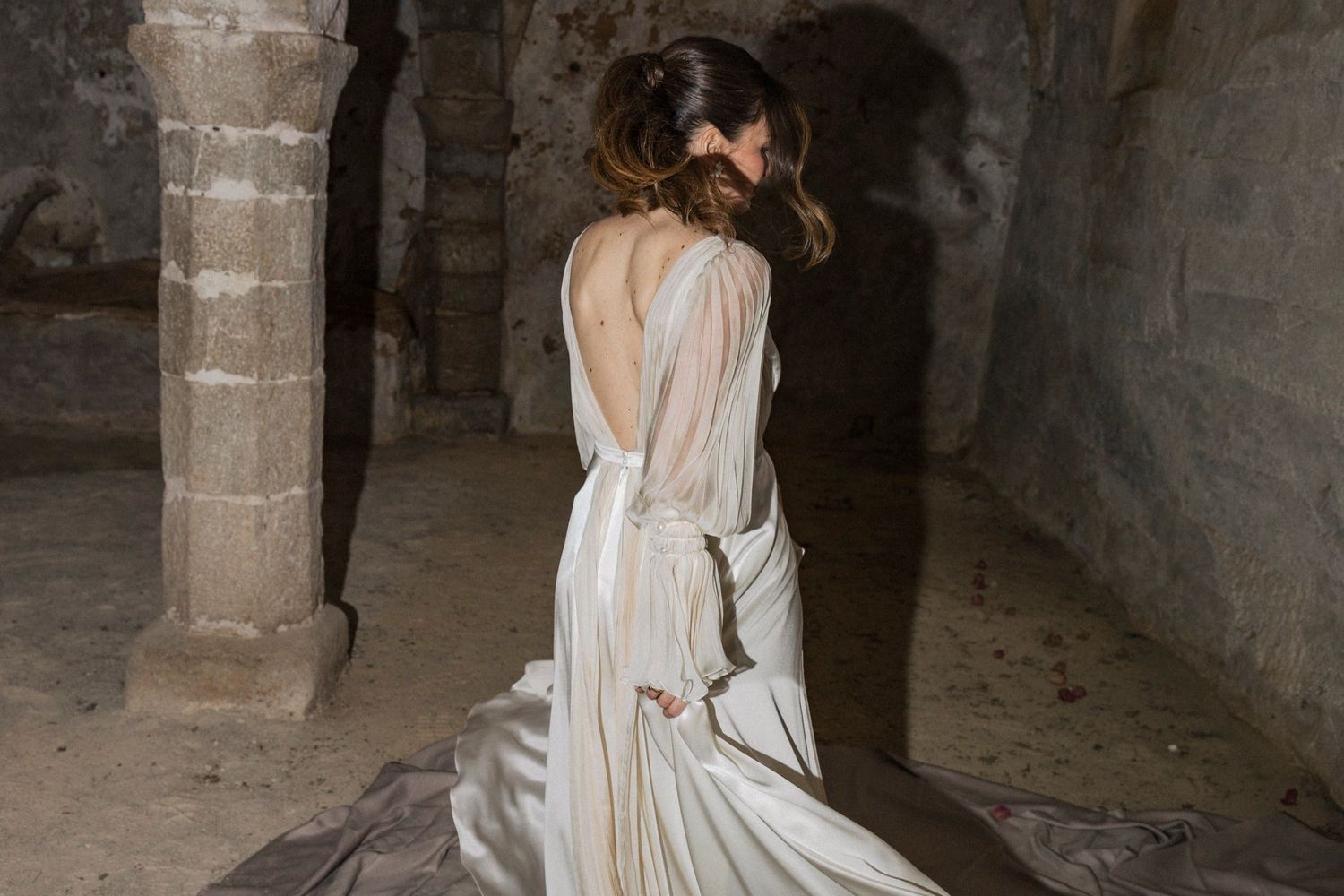 A person in a flowing white dress walks through a dimly lit stone corridor with ancient architectural details.