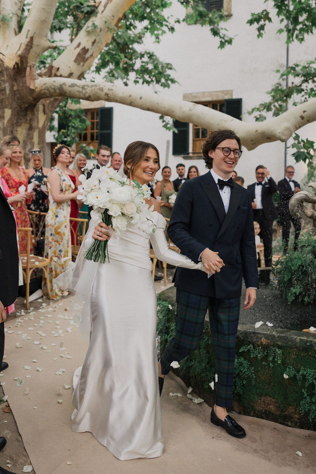 Celebratory wedding moments with flower petals falling in garden courtyard setting.