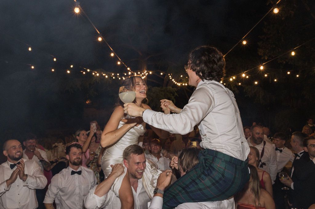 Energetic crowd dancing and celebrating at a nighttime outdoor party under string lights.
