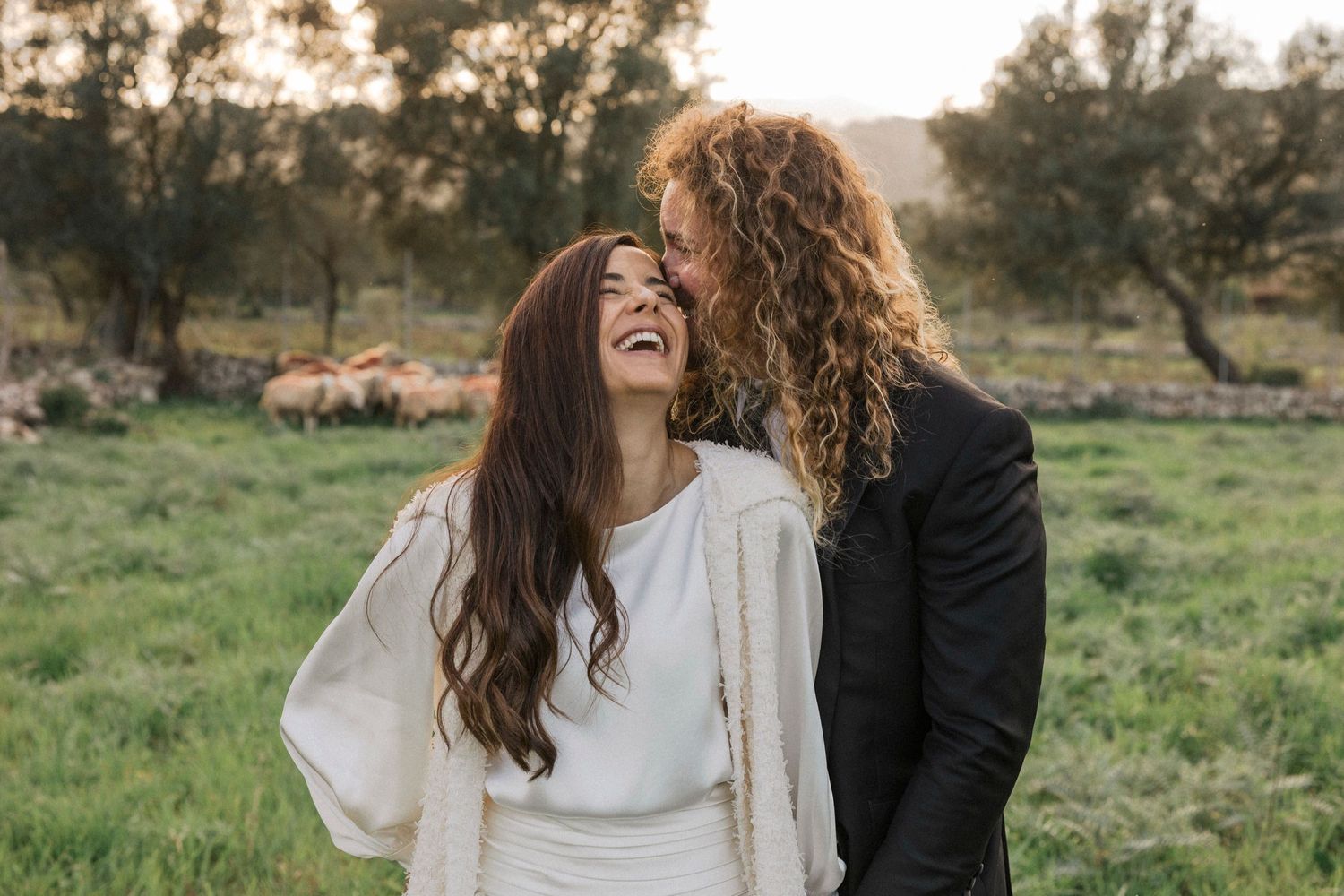 A couple shares a joyful moment together in a scenic outdoor setting with trees and grass.