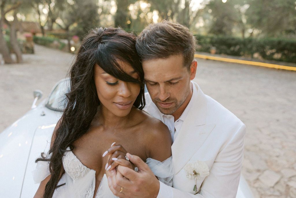 Romantic wedding couple embracing in an outdoor garden setting at sunset.
