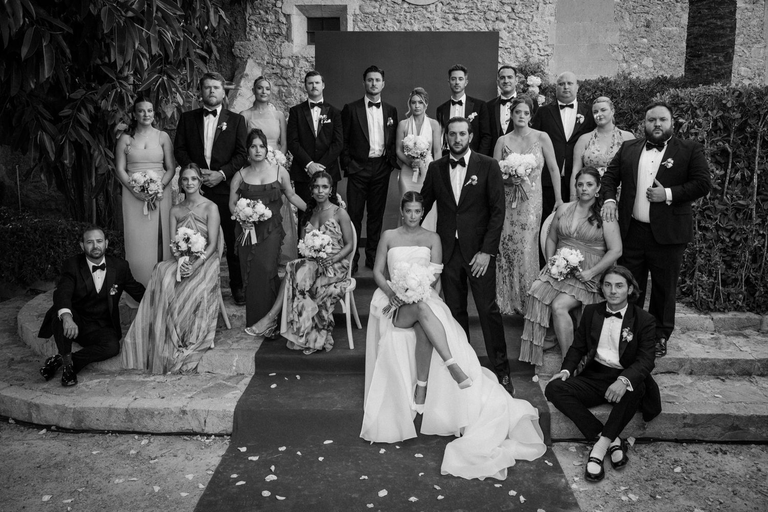 Wedding party celebrates with joyful poses and expressions outside a rustic stone building.
