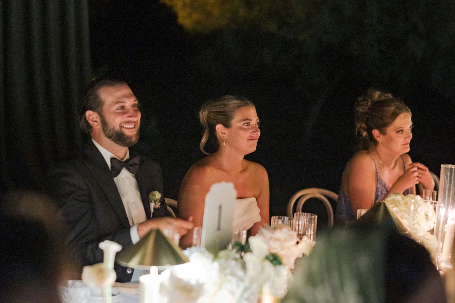 Wedding guests laugh and enjoy themselves at an elegant reception dinner with formal attire and table settings.