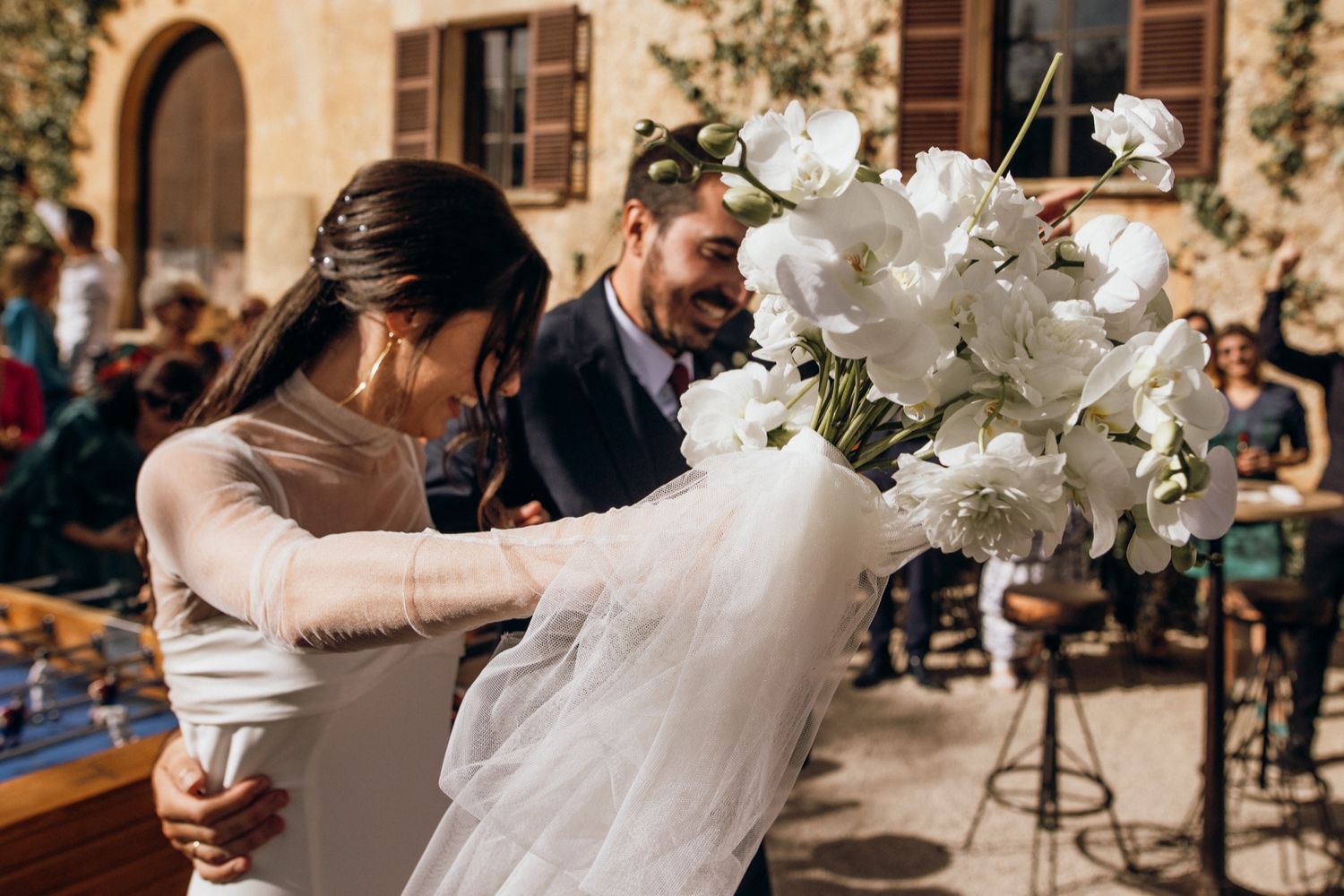 A beautiful white wedding bouquet with flowing veil being arranged at an outdoor venue with stone walls and wooden benches.