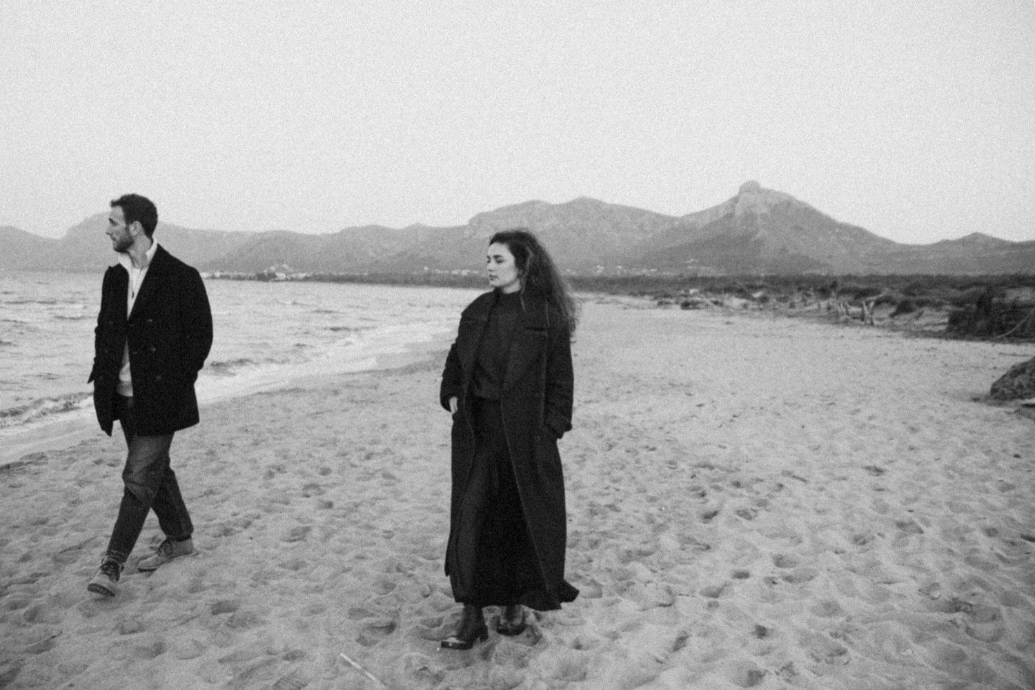 A series of black and white photographs showing people walking along a beach with mountains in the background.