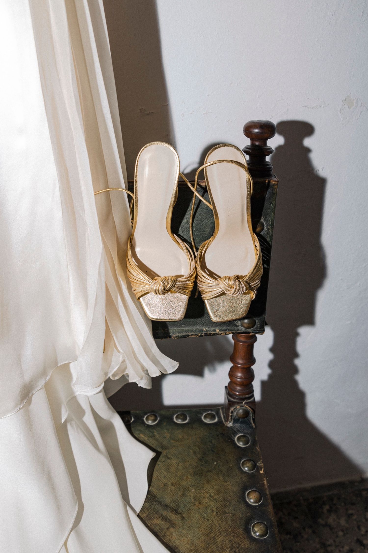 Elegant white bridal shoes displayed on a vintage wooden chair with dramatic shadows.