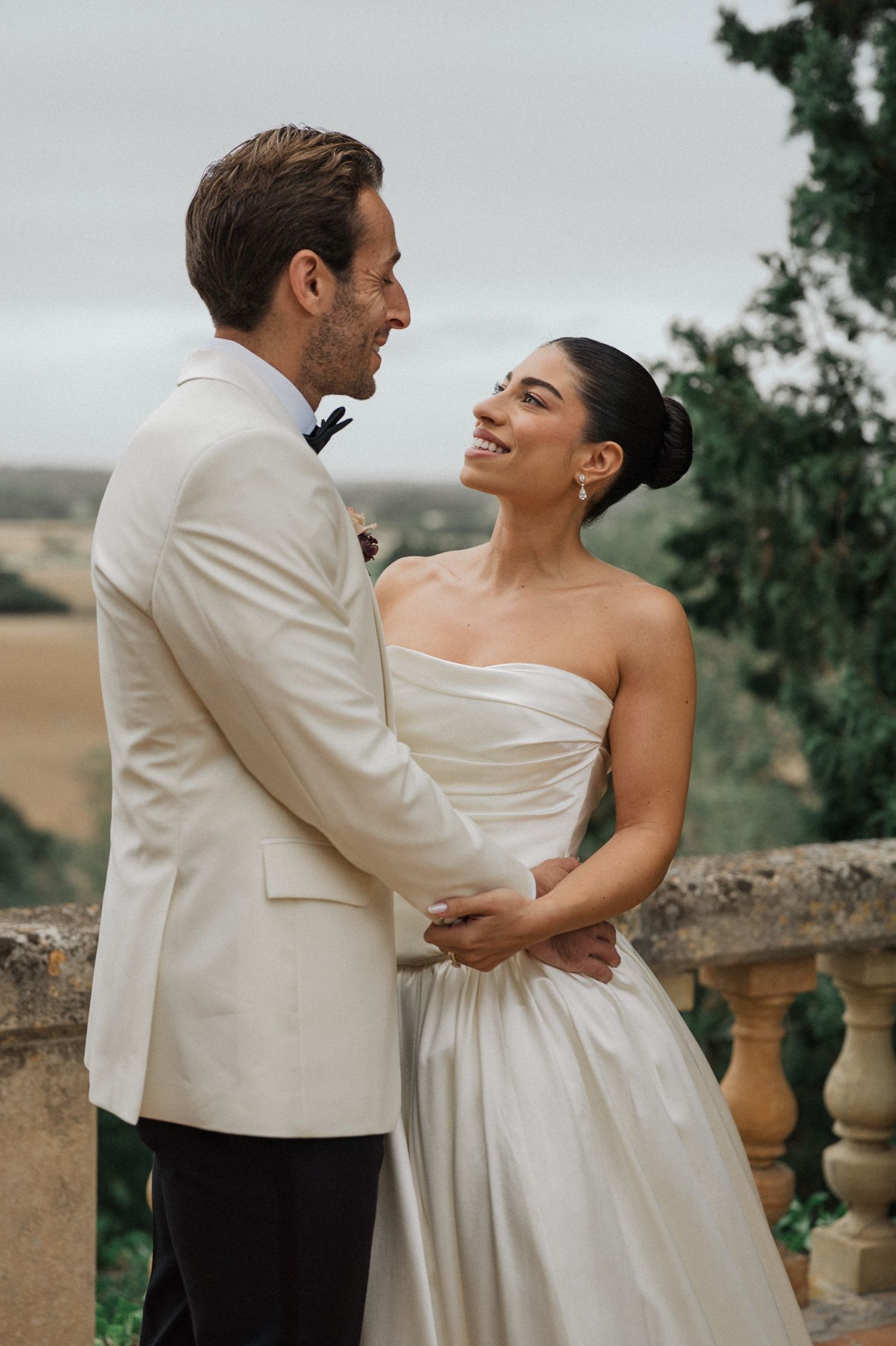 A couple in wedding attire share an intimate dance moment on a scenic terrace overlooking rolling hills.
